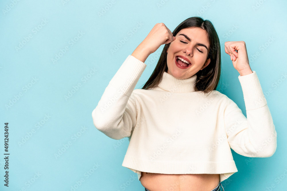 Young caucasian woman isolated on blue background raising fist after a victory, winner concept. Young caucasian woman isolated on blue background raising fist after a victory, winner concept.