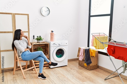 Young latin woman bored waiting for washing machine at laundry room