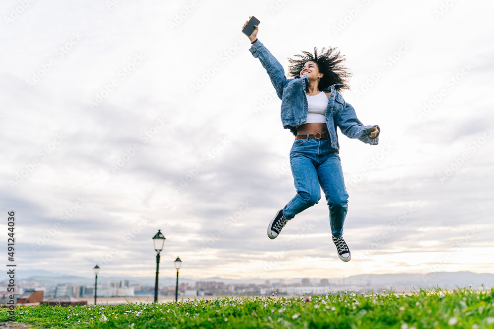 Cheerful woman with smart phone jumping on meadow Cheerful woman with smart phone jumping on meadow