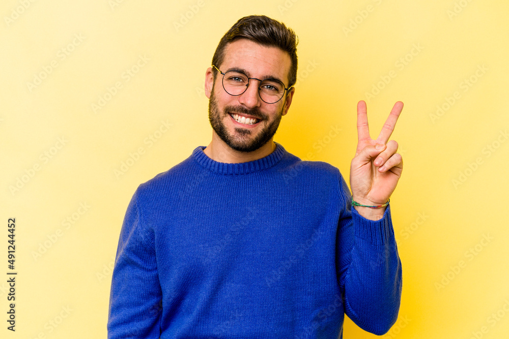 Young caucasian man isolated on yellow background joyful and carefree showing a peace symbol with fingers. Young caucasian man isolated on yellow background joyful and carefree showing a peace symbol with fingers.