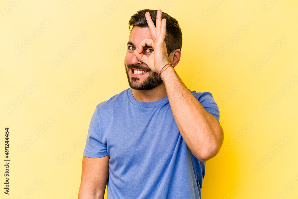 Young caucasian man isolated on yellow background excited keeping ok gesture on eye. Young caucasian man isolated on yellow background excited keeping ok gesture on eye.