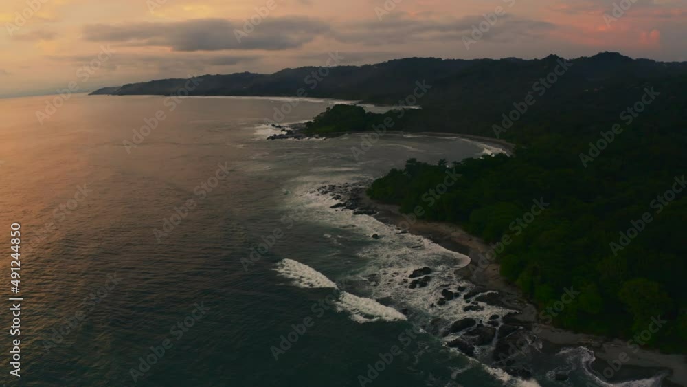 Aerial view around waves hitting rocks at the Playa Mal País beach, evening in Costa Rica - orbit, drone shot Aerial view around waves hitting rocks at the Playa Mal País beach, evening in Costa Rica - orbit, drone shot