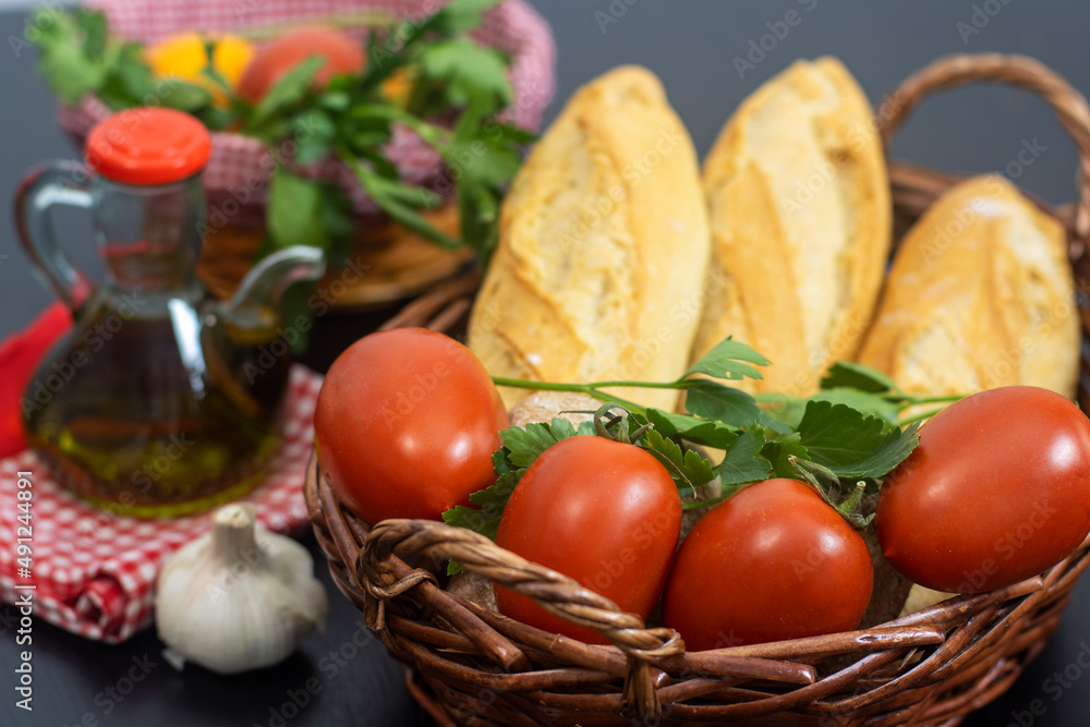 Cesta con pan, tomate y perejil, para preparar un desayuno típico de la zona del Mediterráneo Cesta con pan, tomate y perejil, para preparar un desayuno típico de la zona del Mediterráneo
