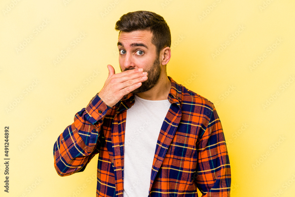 Young caucasian man isolated on yellow background covering mouth with hands looking worried. Young caucasian man isolated on yellow background covering mouth with hands looking worried.