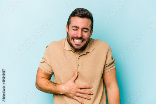 Young caucasian man isolated on blue background touches tummy, smiles gently, eating and satisfaction concept.