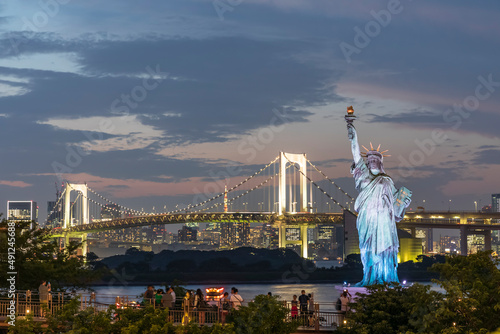 Japan, Kanto Region, Tokyo, Replica of Statue of Liberty and illuminated Rainbow Bridge at dusk photo