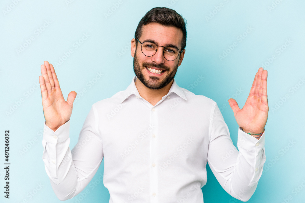 Naklejka premium Young caucasian man isolated on blue background holding something little with forefingers, smiling and confident.