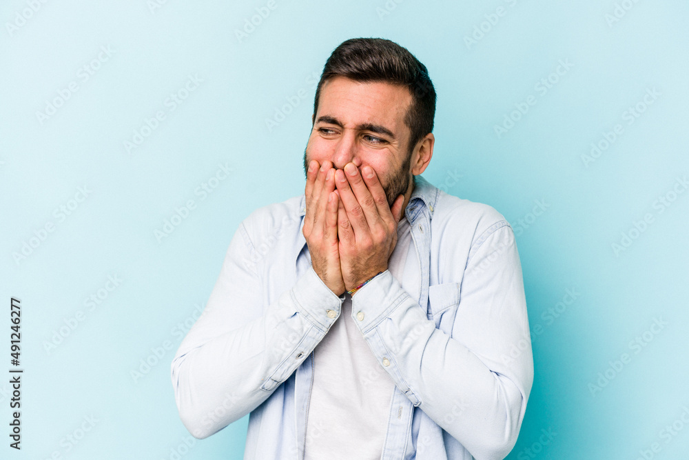 Young caucasian man isolated on blue background laughing about something, covering mouth with hands. Young caucasian man isolated on blue background laughing about something, covering mouth with hands.