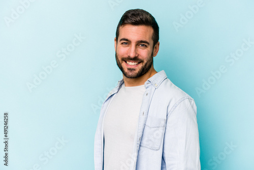 Young caucasian man isolated on blue background confident keeping hands on hips. © Asier