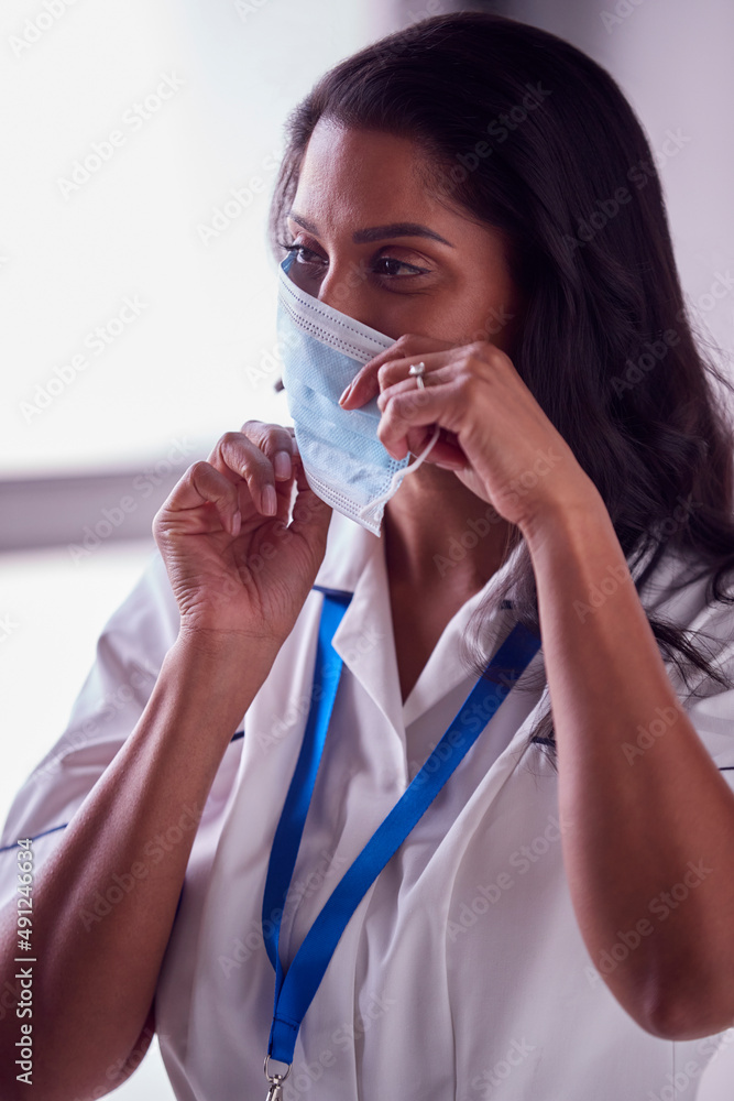 Female Mature Nurse In Uniform Putting On Face Mask In Hospital