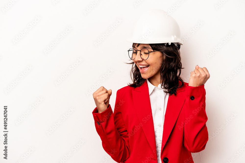 Young architect hispanic woman with helmet isolated on white background raising fist after a victory, winner concept. Young architect hispanic woman with helmet isolated on white background raising fist after a victory, winner concept.