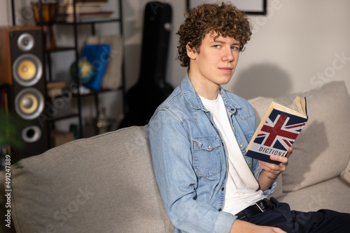 A teenager with curly hair sits focused in a room studying for an English exam. A boy in a blue jean shirt prepares for an English job interview.