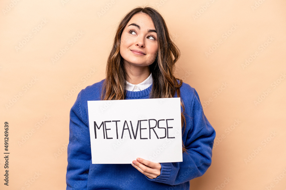 Young caucasian woman holding a metaverse placard isolated on beige background dreaming of achieving goals and purposes Young caucasian woman holding a metaverse placard isolated on beige background dreaming of achieving goals and purposes