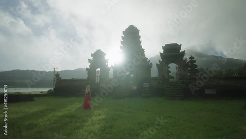 Magical bright sunlight behind Pura Ulun Danu Tamblingan temple with woman in red dress photo