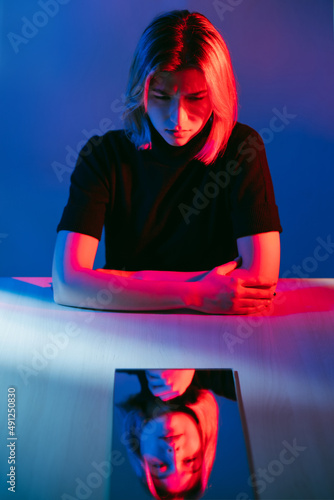 Self analysis. Neon portrait. Mental introversion. Disturbed confused troubled girl with relaxed face mirror reflection in pink blue color light isolated on dark. photo