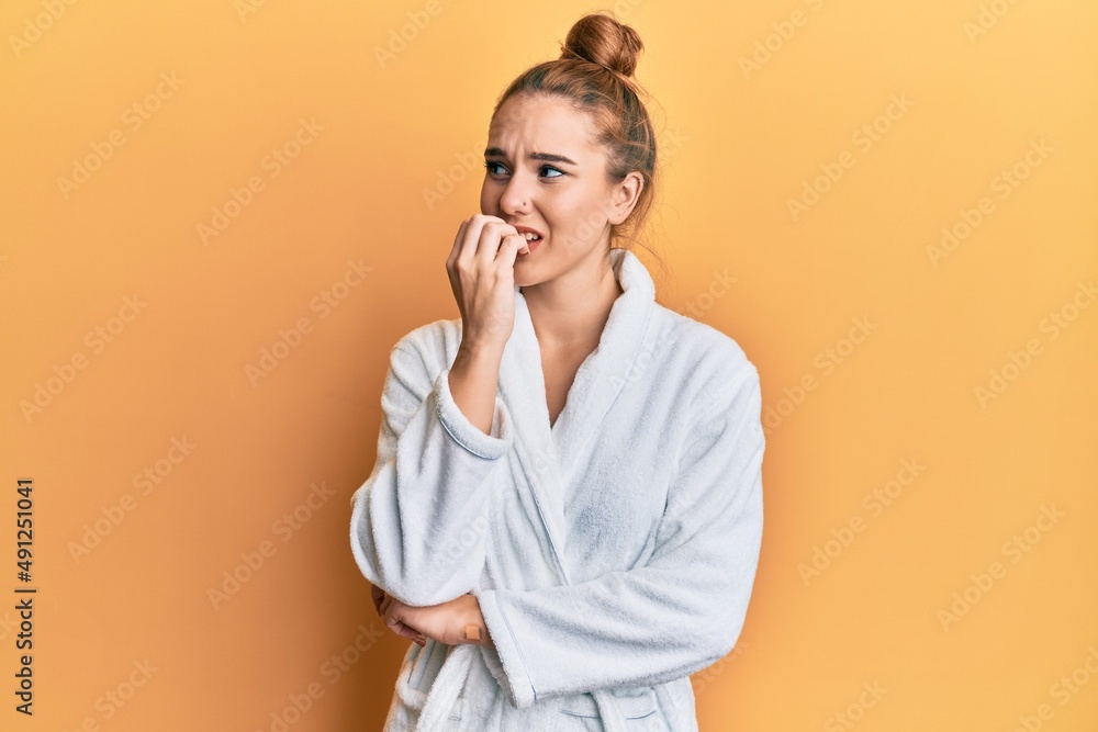 Young blonde woman wearing bathrobe looking stressed and nervous with hands on mouth biting nails. anxiety problem. Young blonde woman wearing bathrobe looking stressed and nervous with hands on mouth biting nails. anxiety problem.
