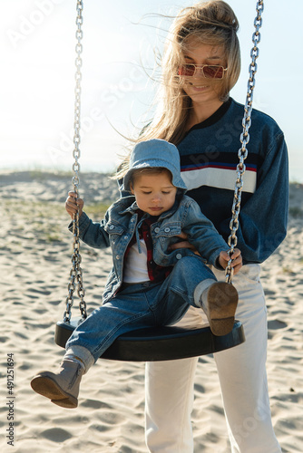 Young mother holding her son sitting on swing at the beach.