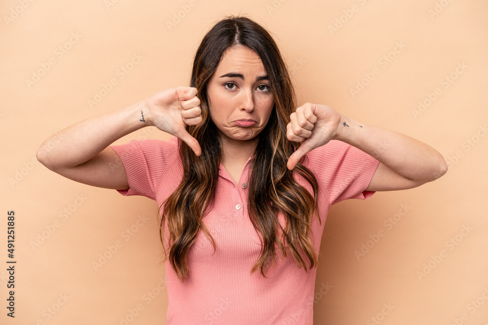 Young caucasian woman isolated on beige background showing a dislike gesture, thumbs down. Disagreement concept.