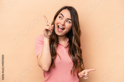 Young caucasian woman isolated on beige background pointing to different copy spaces, choosing one of them, showing with finger. © Asier