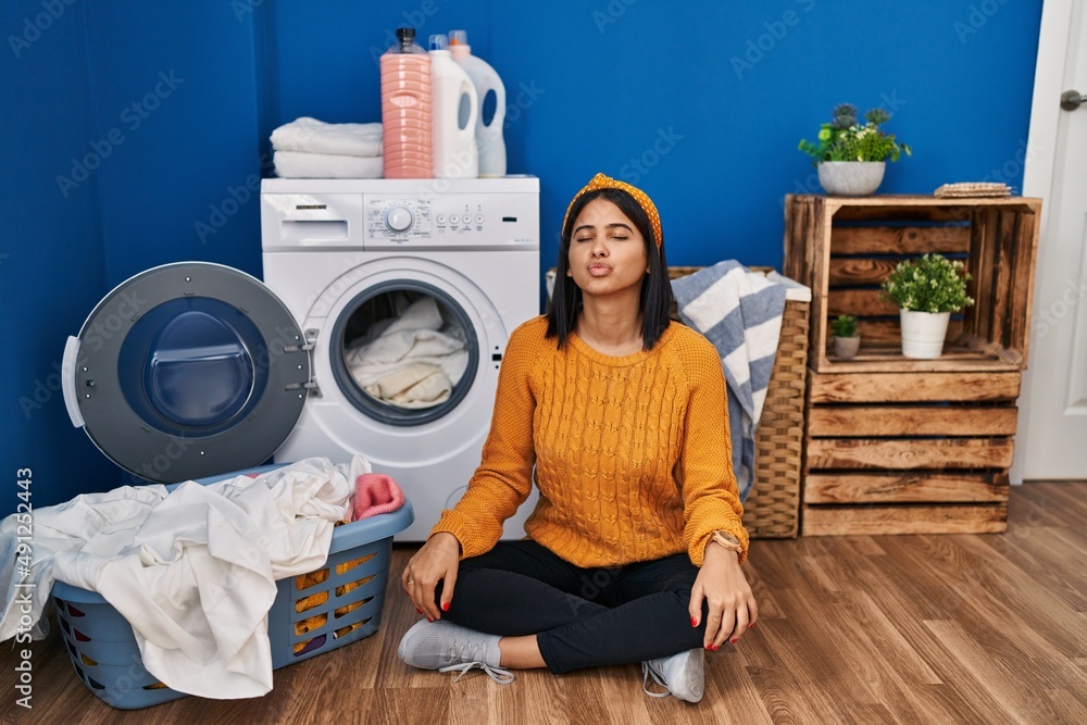 Young hispanic woman doing laundry looking at the camera blowing a kiss on air being lovely and sexy. love expression. Young hispanic woman doing laundry looking at the camera blowing a kiss on air being lovely and sexy. love expression.