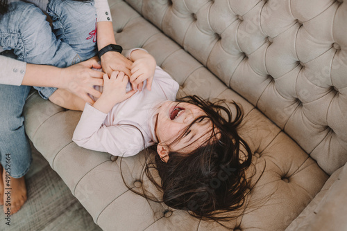 Mother tickling daughter on sofa at home photo