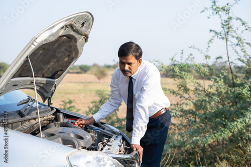 worried businessman checking broken car by lifting car hood on roadside - concept of sadness, worried, accident and problems during road trip