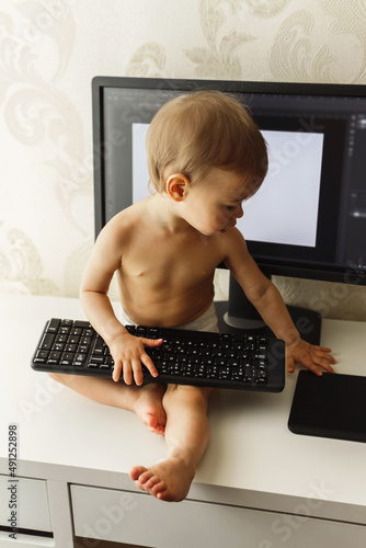 Little boy sitting on a desk and playing with a keyboard. photo