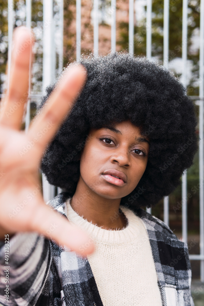 Young afro woman showing palm in front of fence Young afro woman showing palm in front of fence