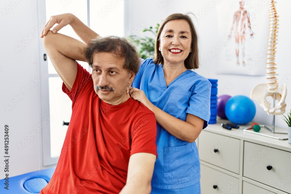 Middle age man and woman wearing physiotherapy uniform having rehab session stretching arm at physiotherapy clinic Middle age man and woman wearing physiotherapy uniform having rehab session stretching arm at physiotherapy clinic