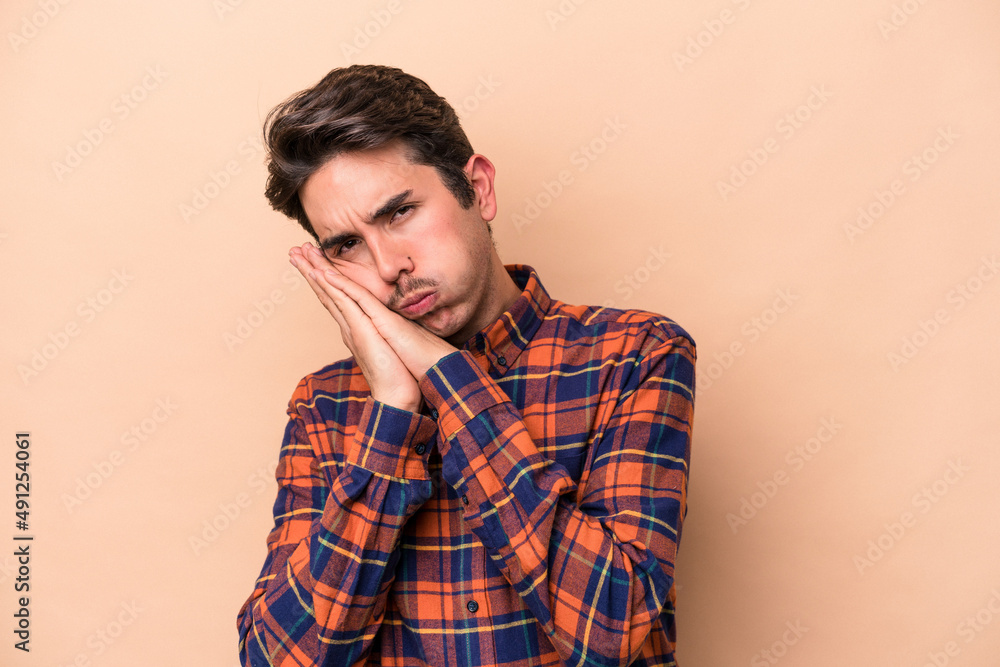 Young caucasian man isolated on beige background yawning showing a tired gesture covering mouth with hand.