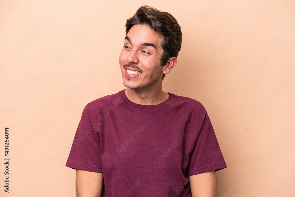 Young caucasian man isolated on beige background laughs and closes eyes, feels relaxed and happy. Young caucasian man isolated on beige background laughs and closes eyes, feels relaxed and happy.