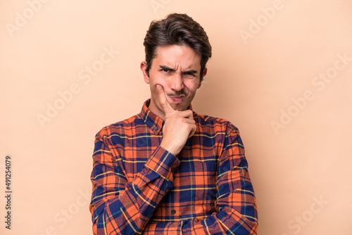 Young caucasian man isolated on beige background unhappy looking in camera with sarcastic expression.
