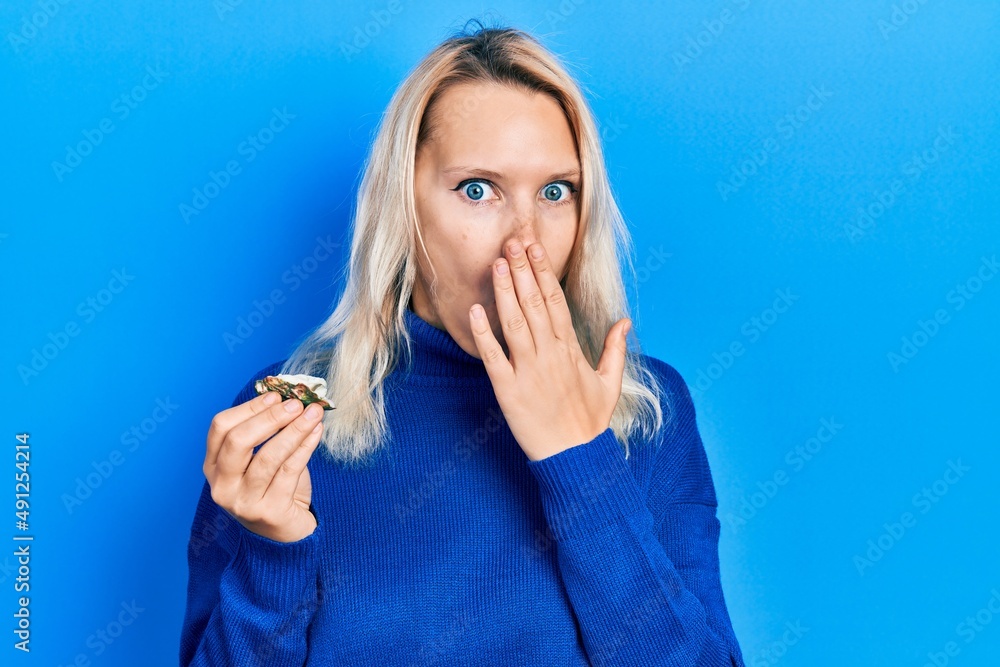 Beautiful caucasian blonde woman holding raw oyster covering mouth with hand, shocked and afraid for mistake. surprised expression Beautiful caucasian blonde woman holding raw oyster covering mouth with hand, shocked and afraid for mistake. surprised expression