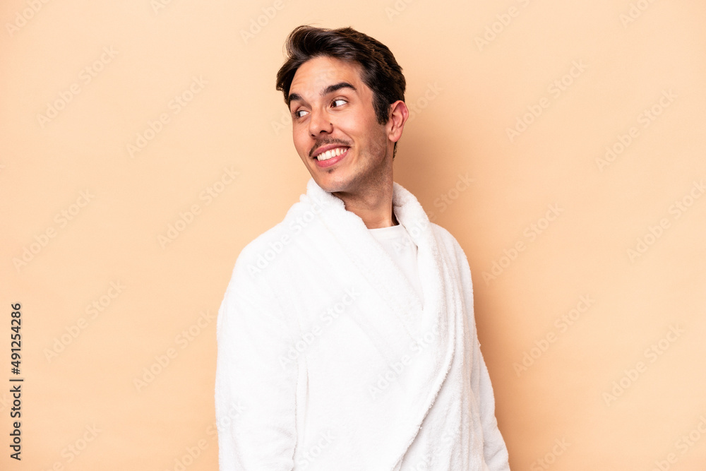 Young caucasian man wearing a bathrobe isolated on beige background looks aside smiling, cheerful and pleasant. Young caucasian man wearing a bathrobe isolated on beige background looks aside smiling, cheerful and pleasant.