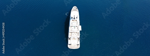 Aerial drone ultra wide top down photo of large yacht with wooden deck anchored in Aegean island deep blue sea visited by tender power boat