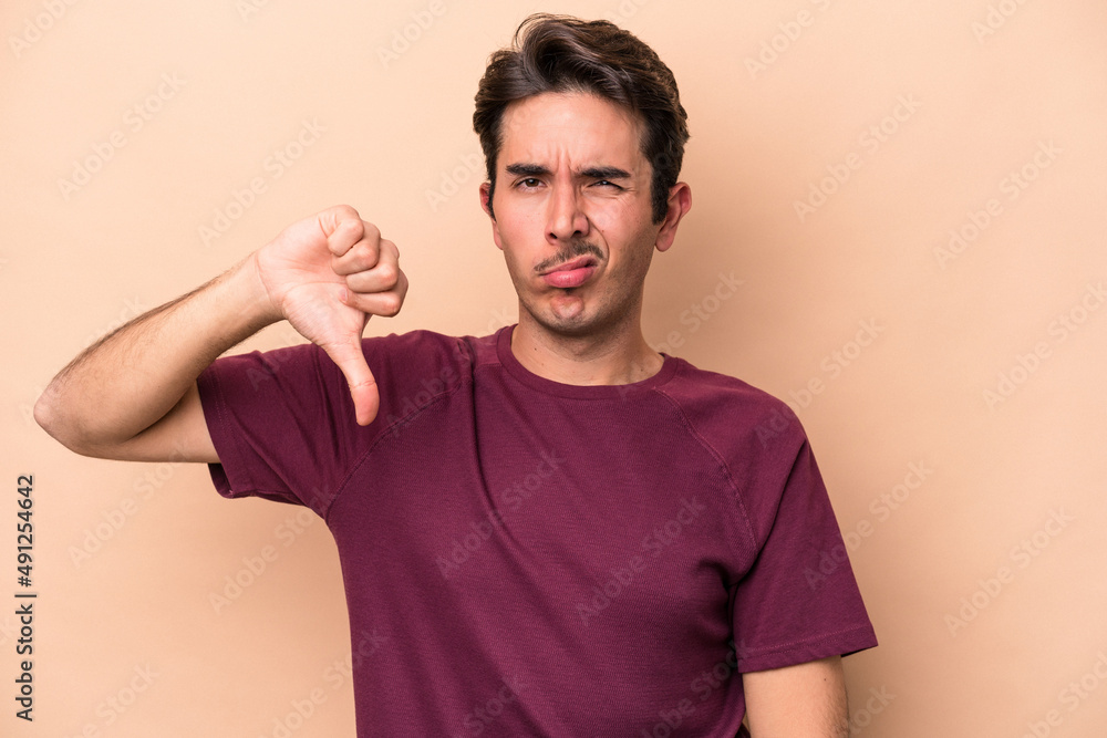 Young caucasian man isolated on beige background showing thumb down, disappointment concept. Young caucasian man isolated on beige background showing thumb down, disappointment concept.