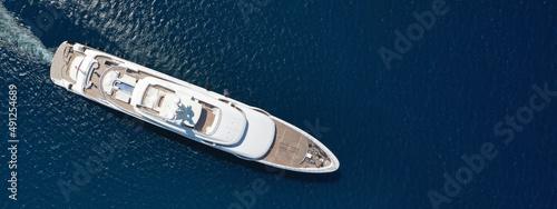 Aerial drone ultra wide top down photo of large yacht with wooden deck anchored in Aegean island deep blue sea visited by tender power boat © aerial-drone