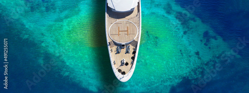 Aerial drone ultra wide top down photo of luxury exotic yacht nose with wooden deck anchored in paradise turquoise bay