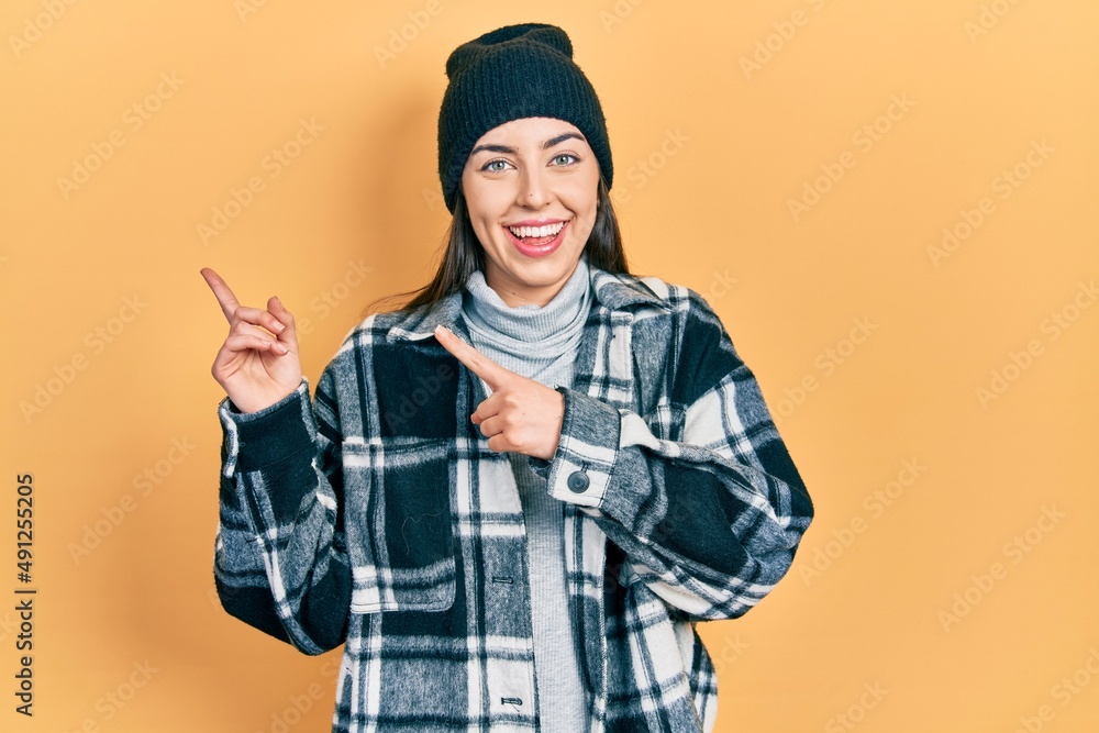 Beautiful woman with blue eyes wearing wool cap smiling and looking at the camera pointing with two hands and fingers to the side. Beautiful woman with blue eyes wearing wool cap smiling and looking at the camera pointing with two hands and fingers to the side.