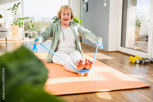 Smiling senior woman exercising with resistance band at home photo