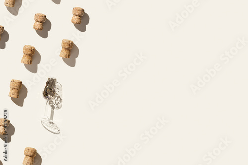 Creative pattern with champagne corks and festive wine glass with sparkles on beige background with hard light and shadows at sunlight. Minimal trend layout, bottle cap from sparkling wine