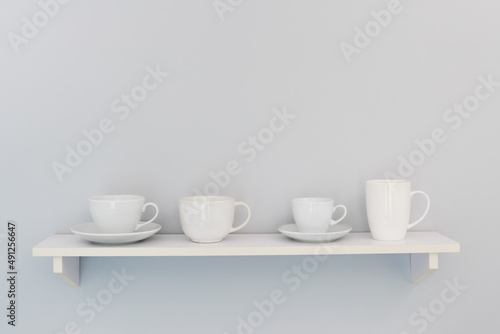 Four white cups on a white shelf