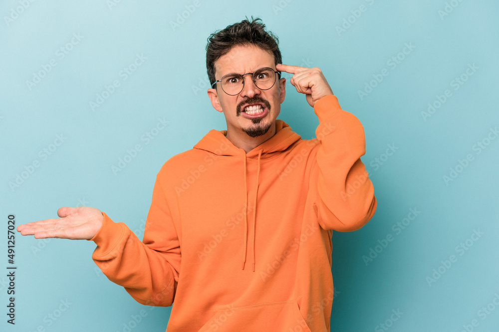 Young caucasian man isolated on blue background holding and showing a product on hand. Young caucasian man isolated on blue background holding and showing a product on hand.