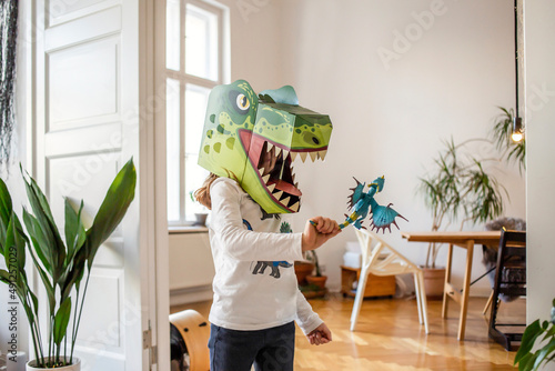 Girl wearing dinosaur mask playing with figurine at home photo