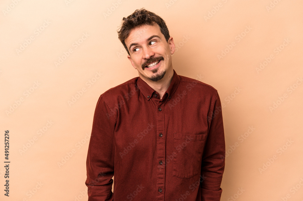 Obraz premium Young caucasian man isolated on beige background laughs and closes eyes, feels relaxed and happy.