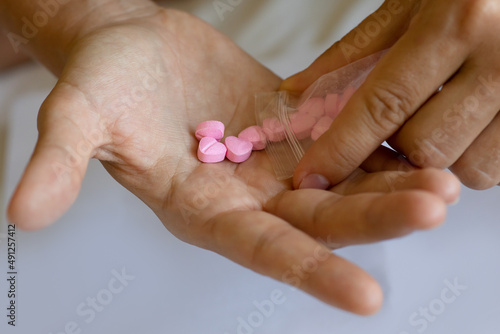 Man pouring heart shaped pills on palm from ziplock bag.