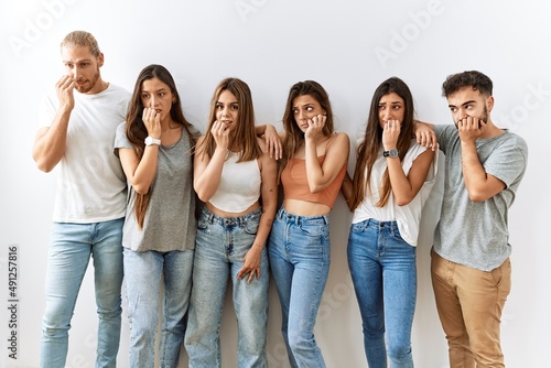 Group of young friends standing together over isolated background looking stressed and nervous with hands on mouth biting nails. anxiety problem.