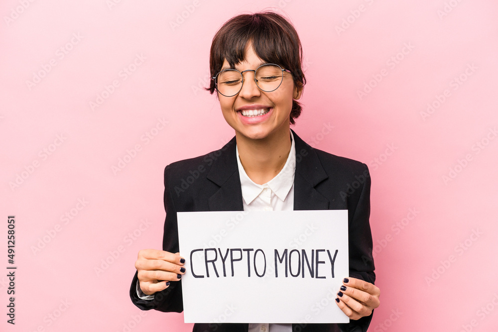 Young hispanic business woman holding a crypto money placard isolated on pink background laughing and having fun. Young hispanic business woman holding a crypto money placard isolated on pink background laughing and having fun.