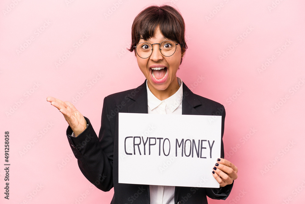 Young hispanic business woman holding a crypto money placard isolated on pink background receiving a pleasant surprise, excited and raising hands. Young hispanic business woman holding a crypto money placard isolated on pink background receiving a pleasant surprise, excited and raising hands.