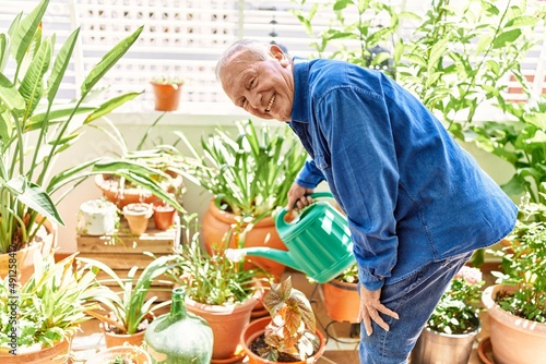 Bild auf Leinwand Senior caucasian man smiling happy watering plants standing at the terrace